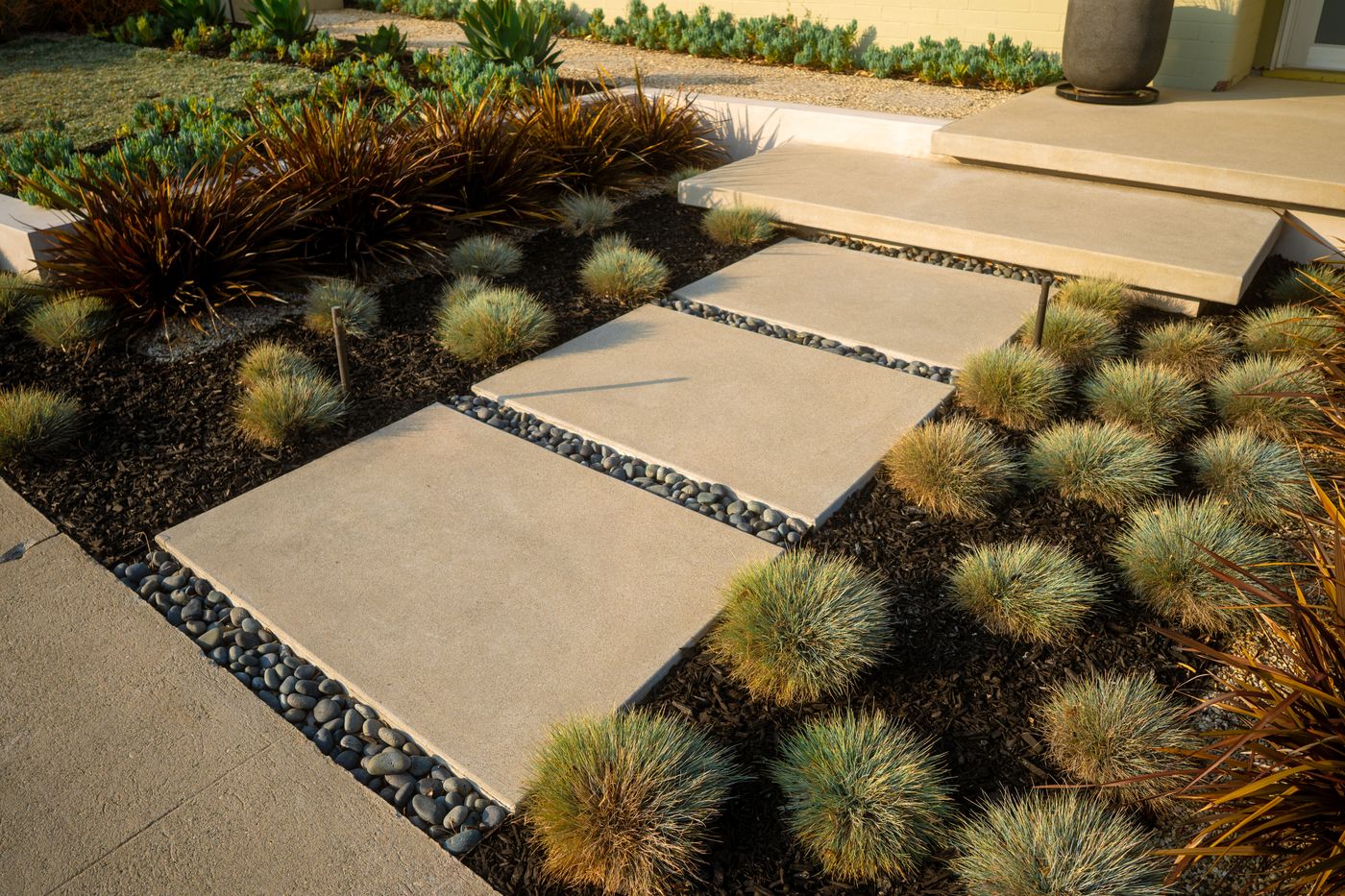 Low-maintenance front entry with concrete stepping pads, river rock, and ornamental grasses